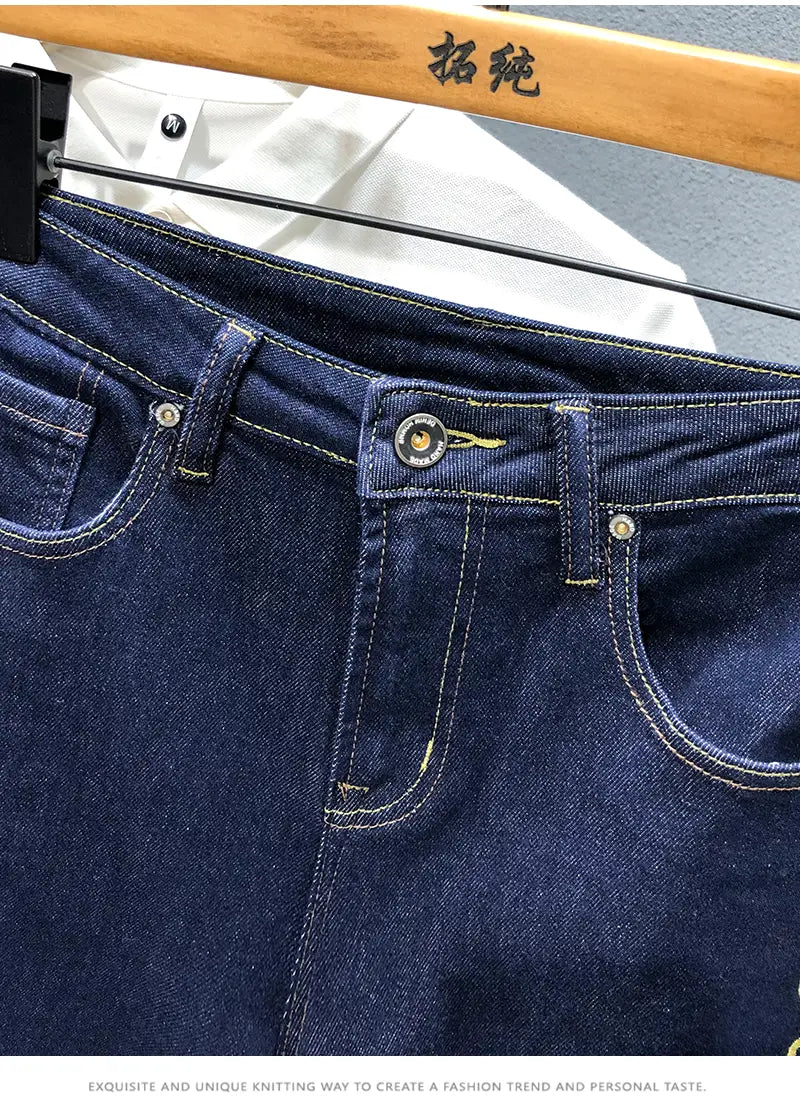 Men slim fit stretch embroidered white denim jeans shown in dark blue denim with contrasting light stitching and silver toned metal hardware.