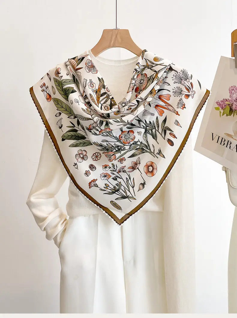 A delicate ivory silk floral square scarf featuring a detailed botanical print in soft earthy tones and a subtle gold border.