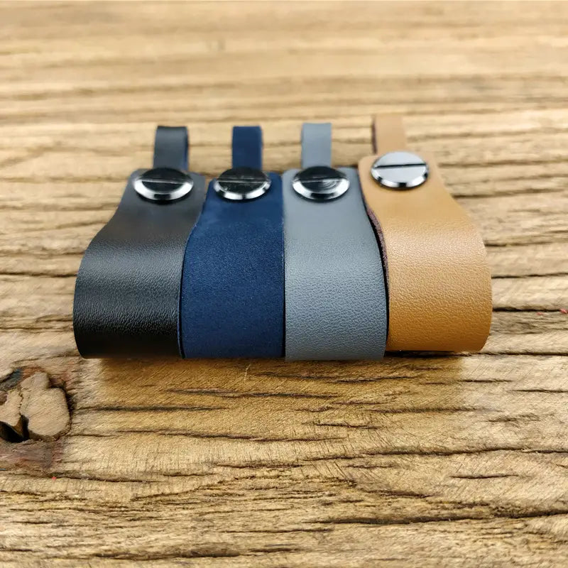 Four genuine leather car keychains in black navy blue gray and tan with silver toned metal key ring clasps.