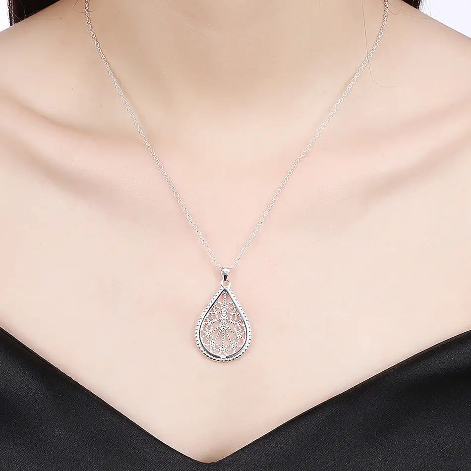 Collier pendentif en forme de goutte en argent sterling présentant un design filigrané complexe avec un bord rehaussé de petites perles, dans un ensemble de bijoux délicat.