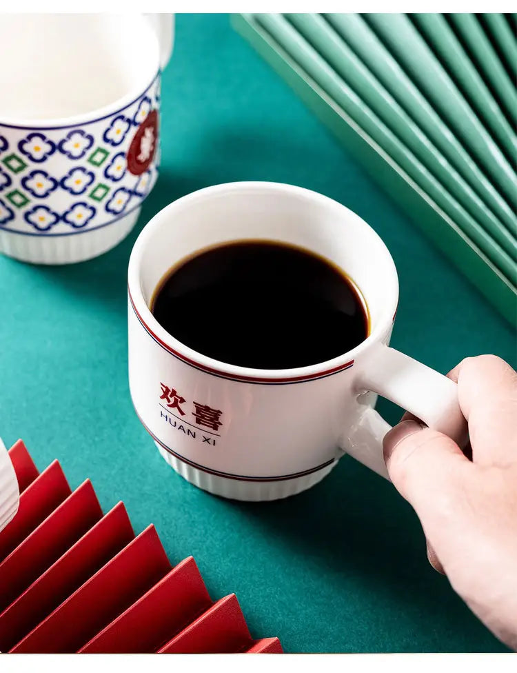 Tasse en céramique blanche présentant des caractères chinois rouges et un fin liseré rouge, remplie de café foncé, dans le coffret cadeau de deux tasses de couple en céramique pour mariage chinois.
