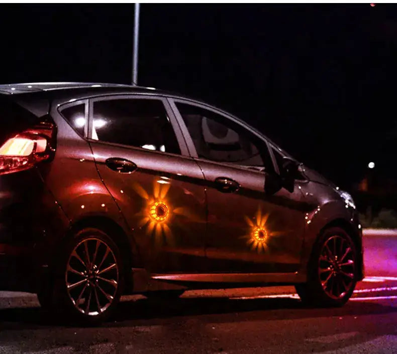 a glowing orange sun-shaped magnetic led roadside emergency strobe light decal is attached to the side of a dark-colored car.