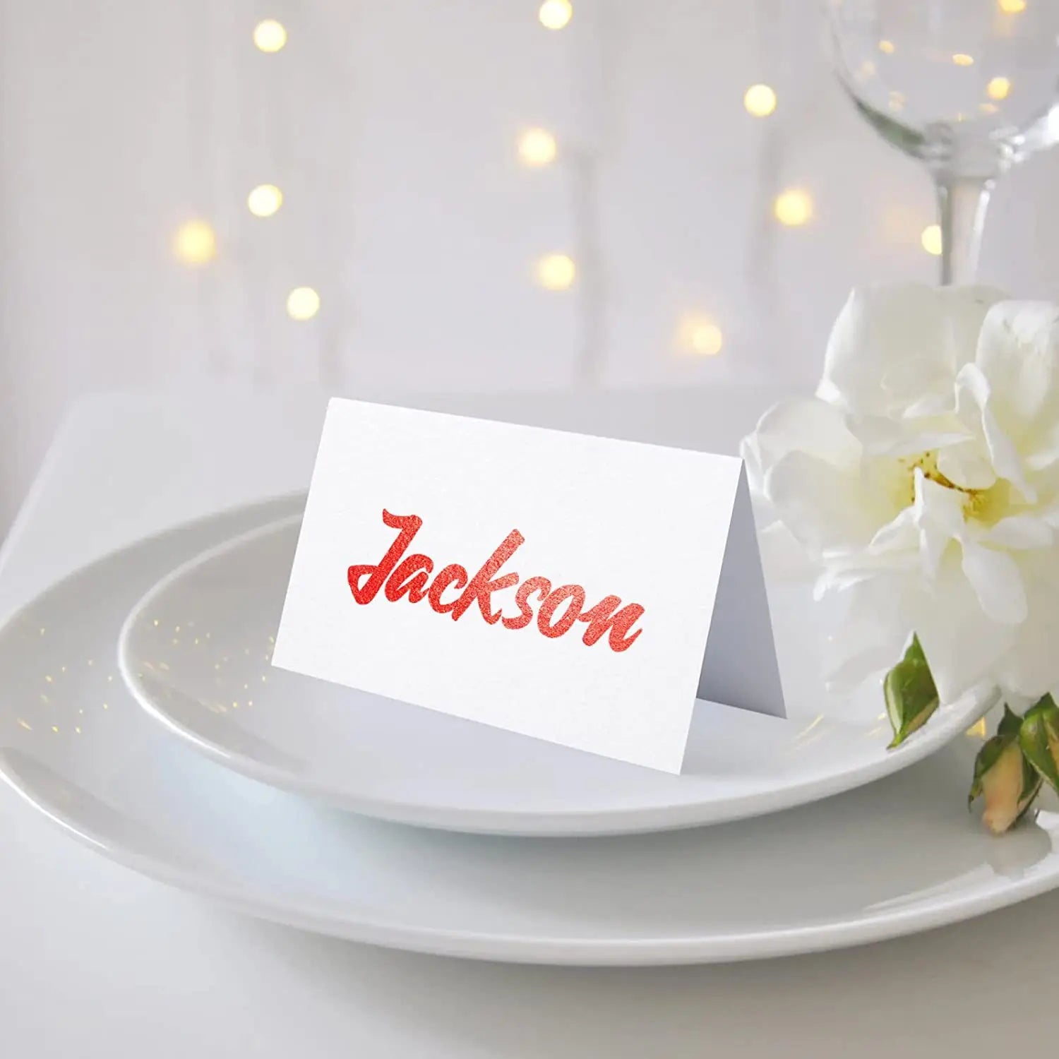 ウェディングテーブル着席用の、白い紙製ユーカリの葉のプレースカード。名「jackson」を、きらめく赤の筆記体で印刷しています。