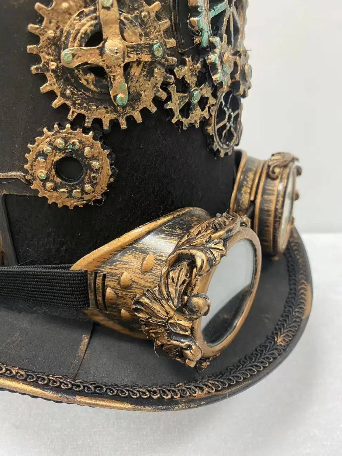 Black steampunk top hat made of leather adorned with brass gears and ornate goggles for a vintage industrial look.