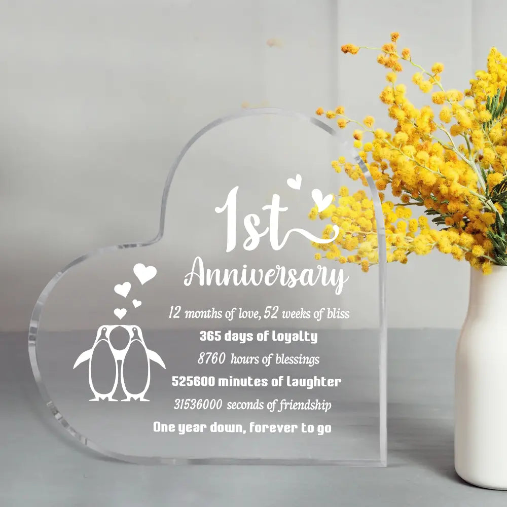 Plaque d’anniversaire d’un an en forme de cœur en acrylique transparent, avec texte blanc gravé et un motif de pingouin.