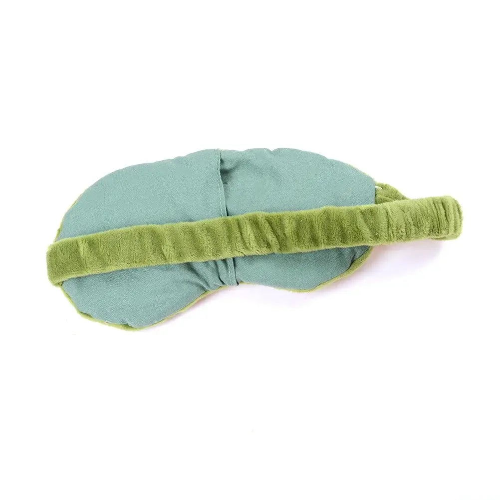 Una máscara de ojos de felpa color verde salvia, suave, con una diadema aterciopelada a juego, mostrada como producto terminado para su uso como máscara de dormir de rana inspirada en dibujos animados.