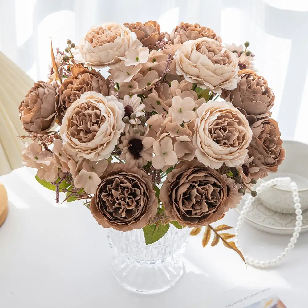 Ein zarter Strauß aus künstlichen Blumen mit Seidenpfingstrosen und Hortensien in sanften Beige-Taupe- und Cremetönen, in einer klaren Kristallvase für die Wohnraumdekoration angeordnet.