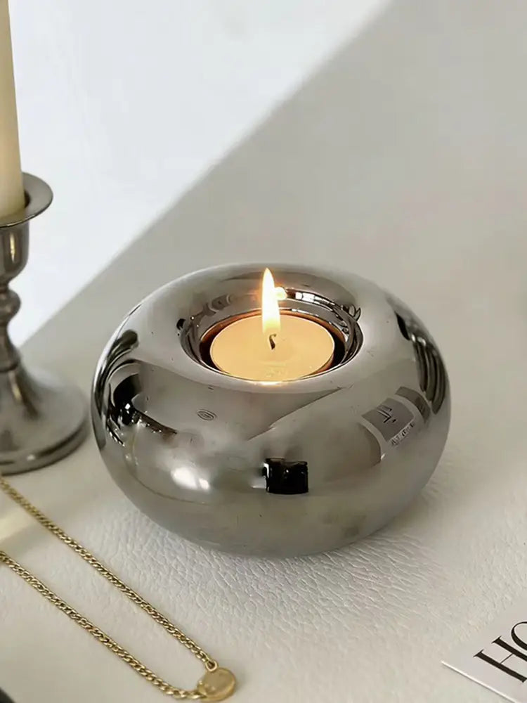 Silver ceramic sphere candle holder made of shiny silver metallic material with a smooth rounded design holding a lit tea light.