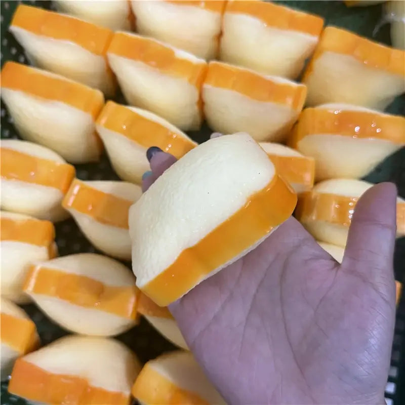 Eine Hand hält einen transparenten, zweifarbigen Butterstick als ASMR-Sensory-Squishy-Spielzeug mit einem glatten weißen Körper und einem glänzenden orangefarbenen Band um die gebogene Kante.