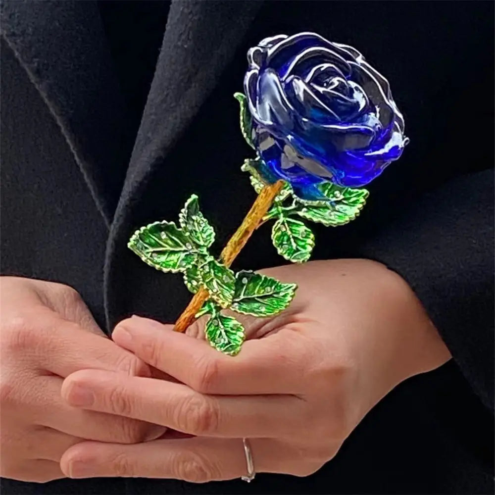 A translucent deep blue crystal glass rose with green metallic leaves and a gold-toned stem held gently in hands for Valentine’s Day gift.