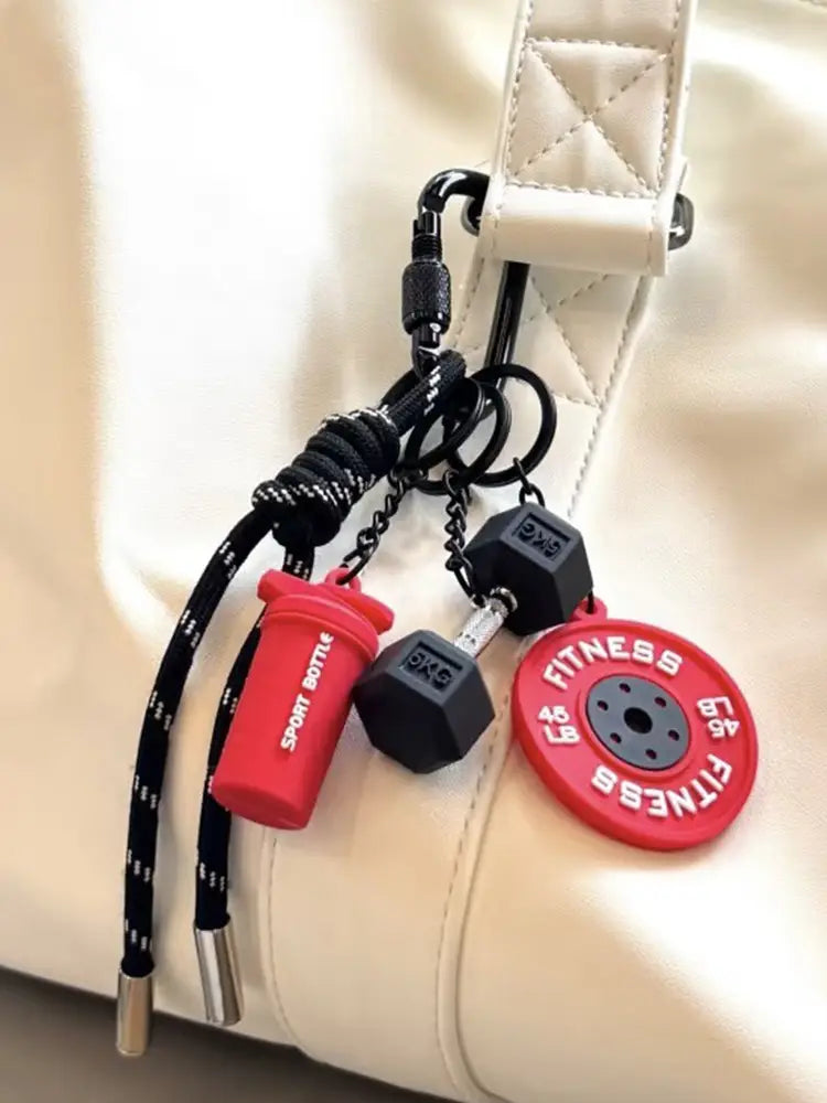 Une breloque pour sac de sport en porte-clés de fitness, représentant un haltère, avec une bouteille shaker en silicone rouge et noire, une haltère en caoutchouc et des breloques de disque de poids.
