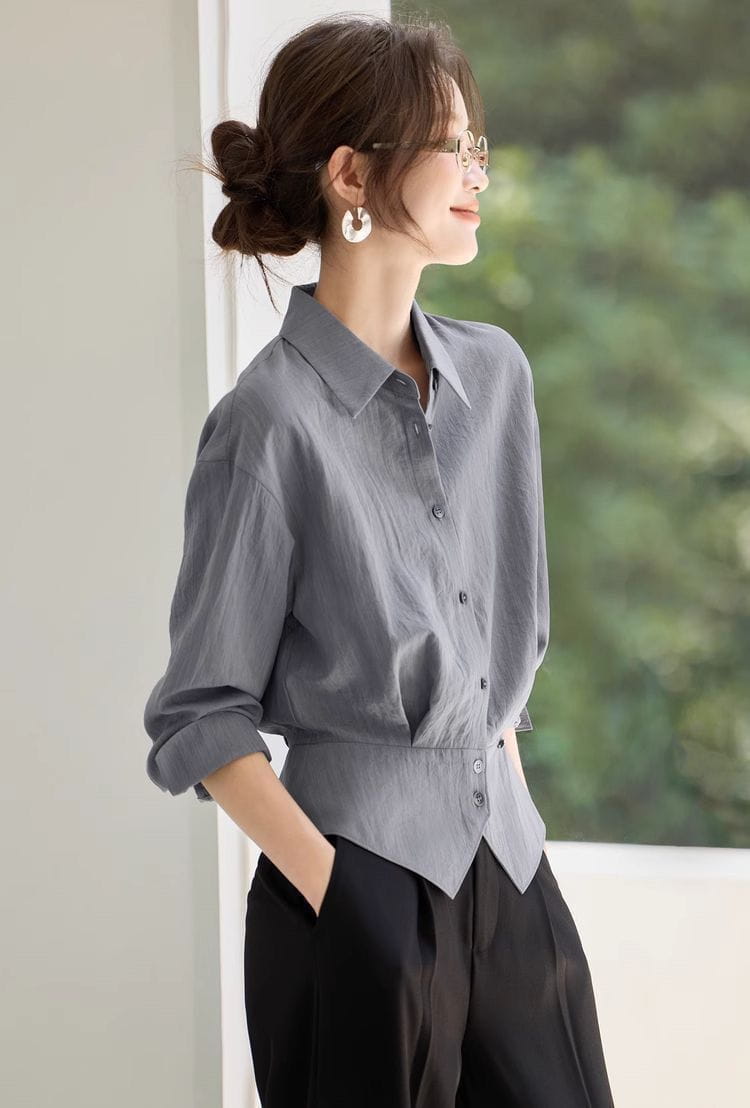 Blouse chemise manches longues grise avec taille cintrée, coupe ajustée et manches retroussées, idéale pour une tenue de bureau.