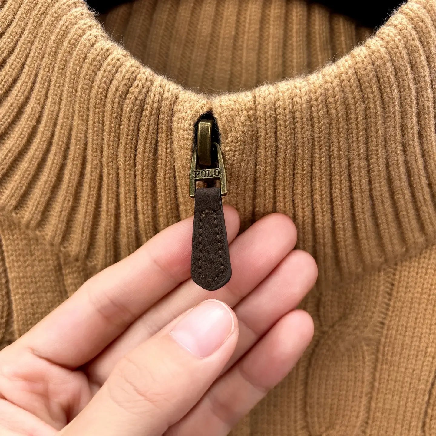 Herren-Designer-Sweater aus Camelfarbenem Zopfmusterstrick mit halbem Reißverschluss, mit braunem Leder-Reißverschluss-Zug und einem Messing-farbenen Metallschieber, der mit „Polo“ graviert ist.