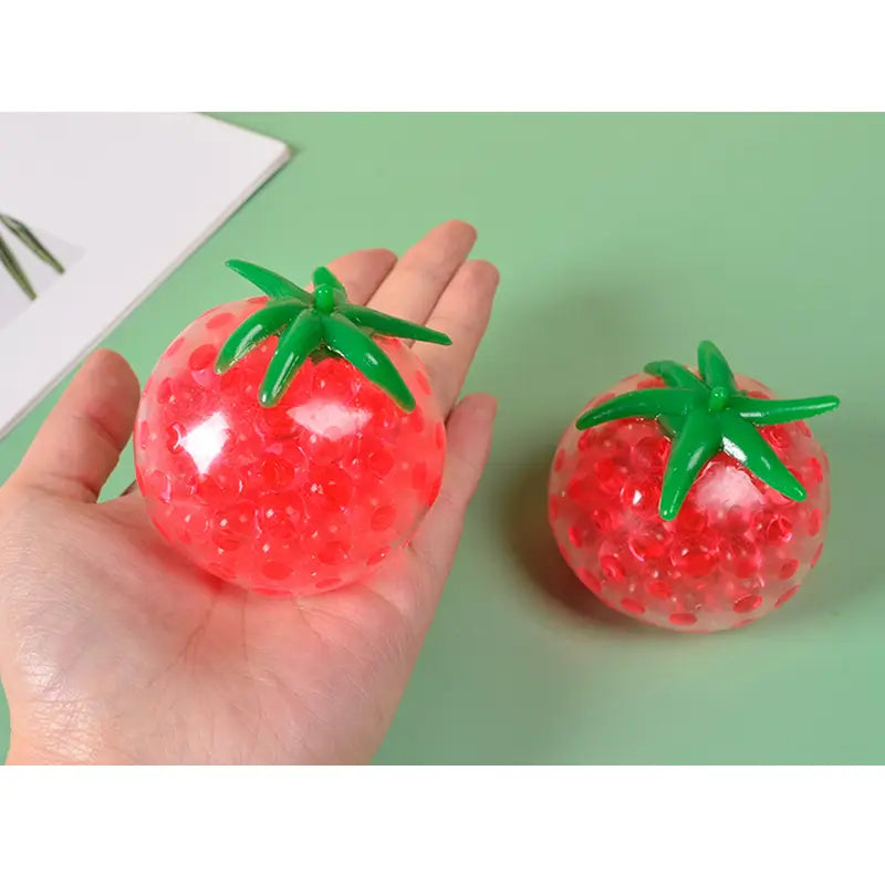 Red tomato-shaped squishy stress relief toy made of translucent gel beads with a green plastic stem for squeezing and stress reduction.