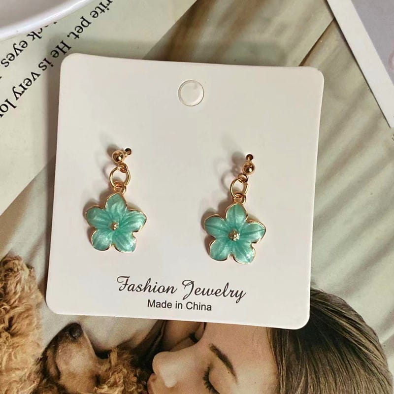 Une paire de boucles d’oreilles délicates en fleur émaillée vert menthe, avec des attaches en métal à l’aspect doré et une minuscule pierre au centre ; complètent un collier pendentif de fleur romantique et mignon avec une chaîne à maillons.