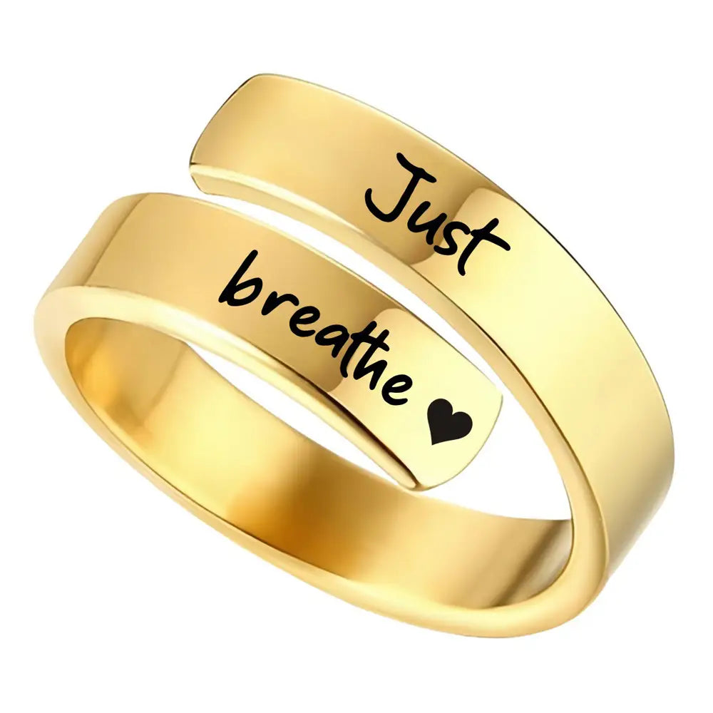 Gold-colored stainless steel wrap-around anxiety ring engraved with just breathe in black script and a small heart symbol.