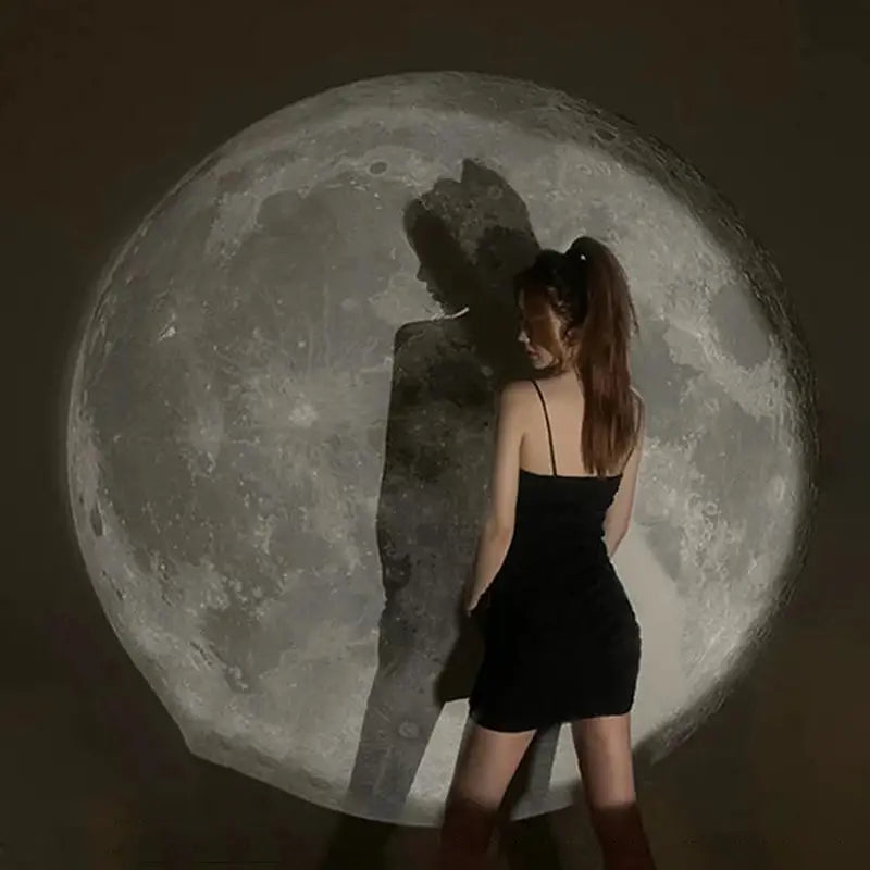 Una mujer con un mini vestido negro sin tirantes se encuentra frente a una gran proyección detallada de la luna creada por una lámpara de proyección USB para luz de estrellas de galaxia de luna y Tierra.
