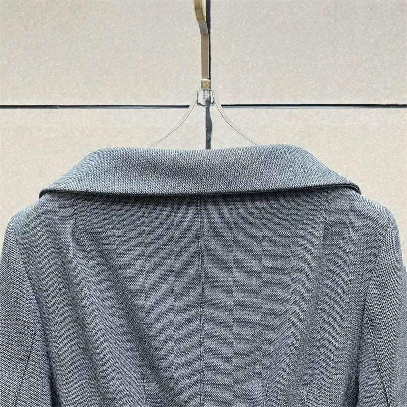 Veste blazer en laine grise texturée, col structuré, suspendue sur un cintre transparent, associée à une jupe crayon grise taille haute de longueur genou au style Y2K