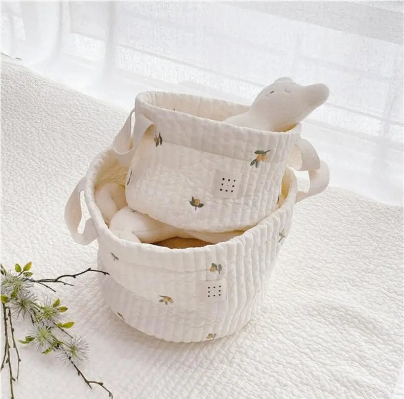 Ein Set aus zwei cremefarbenen gepolsterten Baumwoll-Babywindel-Aufbewahrungskörbchen mit zarter Zitronen- und Blattstickerei sowie weichen Griffen zum einfachen Tragen.