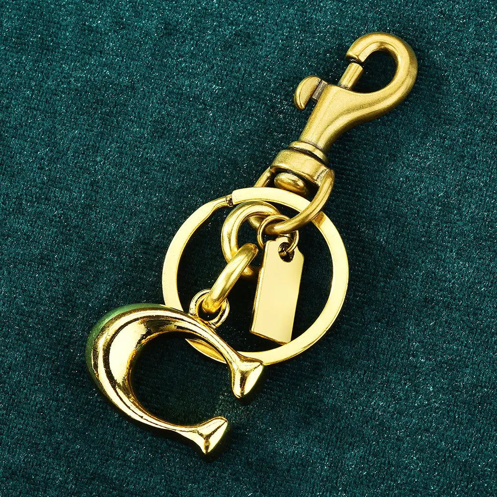 Letter b gold metal keychain featuring a gold-tone metal design with a prominent interlocking c logo, sturdy swivel hook clasp, and attached rectangular tag as a car accessory.