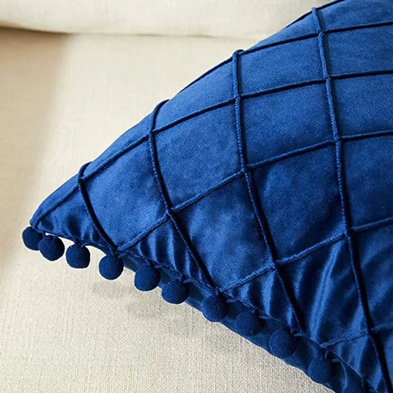 housse de coussin en velours bleu profond avec motif losange matelassé et pompons décoratifs le long du bord, recevant des retours positifs parmi les housses de coussin.