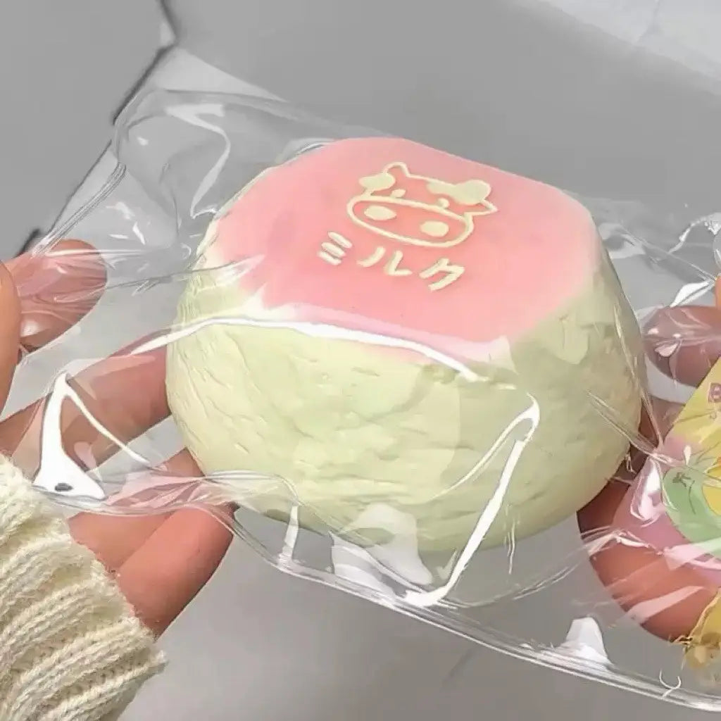Un jouet antistress « squeeze » à couches rose et vert, qui remonte lentement, de type dessert kawaii, avec un motif Hello Kitty sur le dessus, enveloppé dans un plastique transparent pour soulager le stress sensoriel.