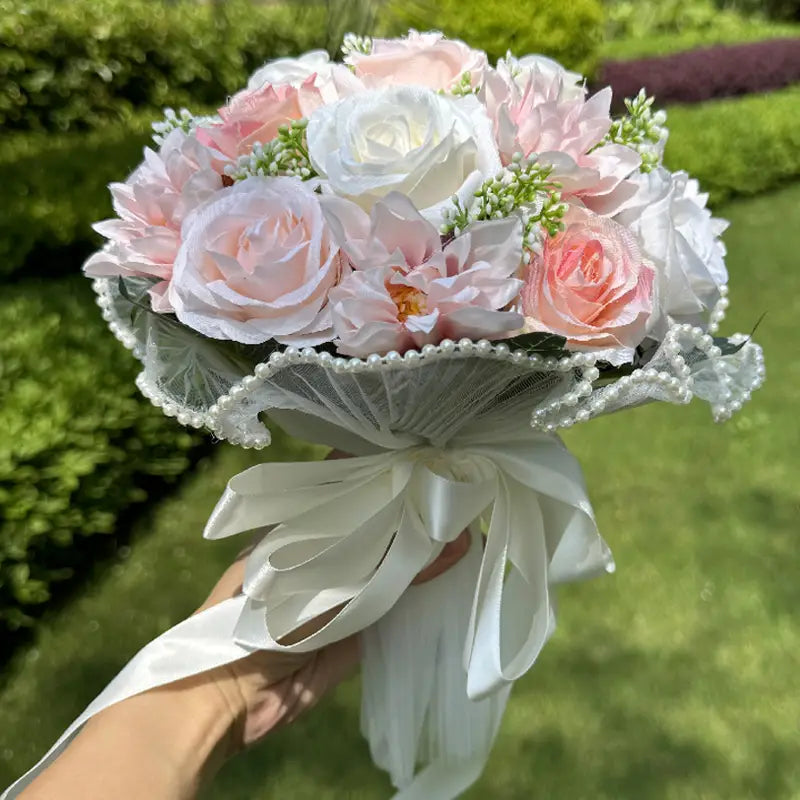 White silk rose wedding bouquet featuring a delicate arrangement of artificial soft pink and white roses wrapped with a sheer lace ribbon adorned with pearls.