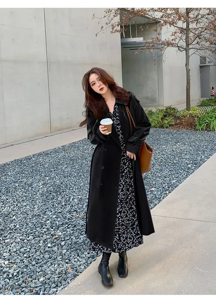 Black double-breasted trench coat with long sleeves worn over a floral dress for casual windbreaker use.