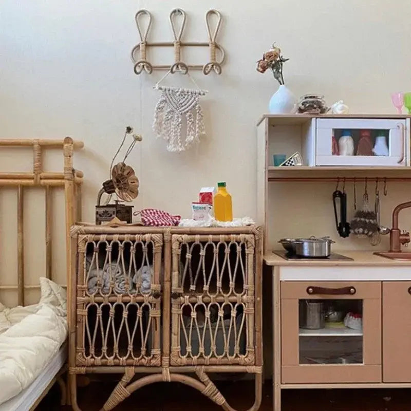 Geflochtenes Spielküchen-Set mit beiger Arbeitsplatte und Holzschränken, dargestellt neben einem Rattan-Kinder-Wandhaken zur Aufbewahrung von Kleidung für die Organisation im Kinderzimmer.