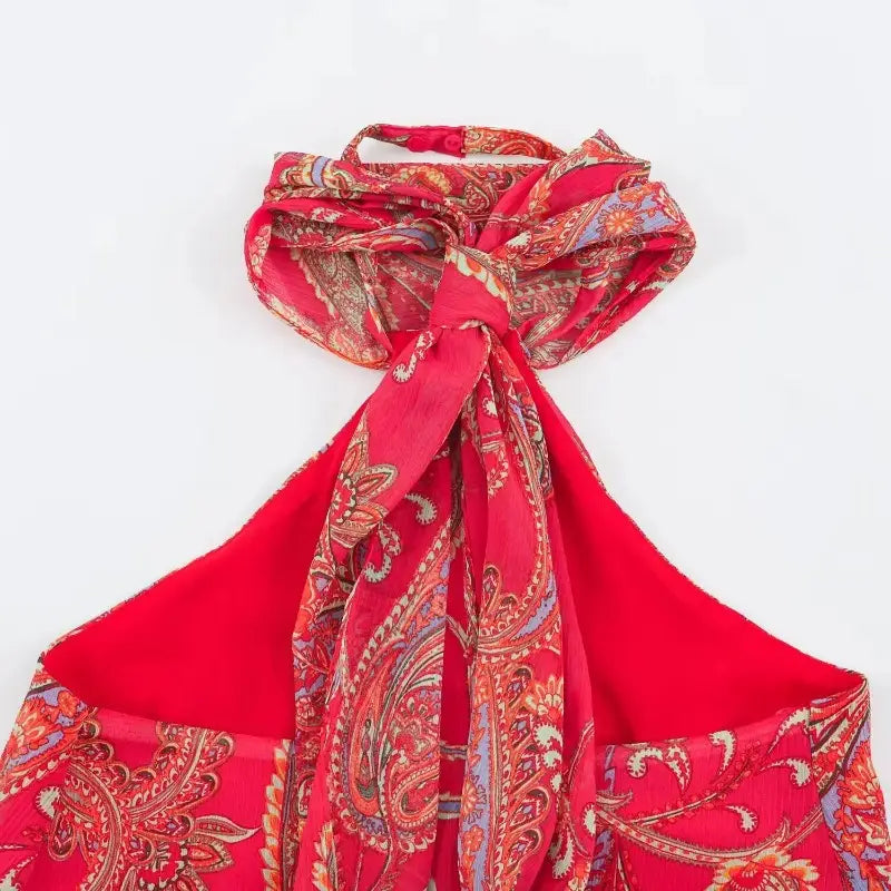 a vibrant red silk halter top with an intricate gold and blue paisley pattern tied into a decorative knot at the neckline paired with a midi skirt set.