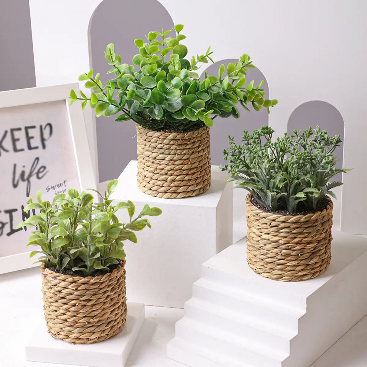three small potted artificial plants featuring green eucalyptus flowers in woven natural fiber pots with a textured braided design measuring 17cm.