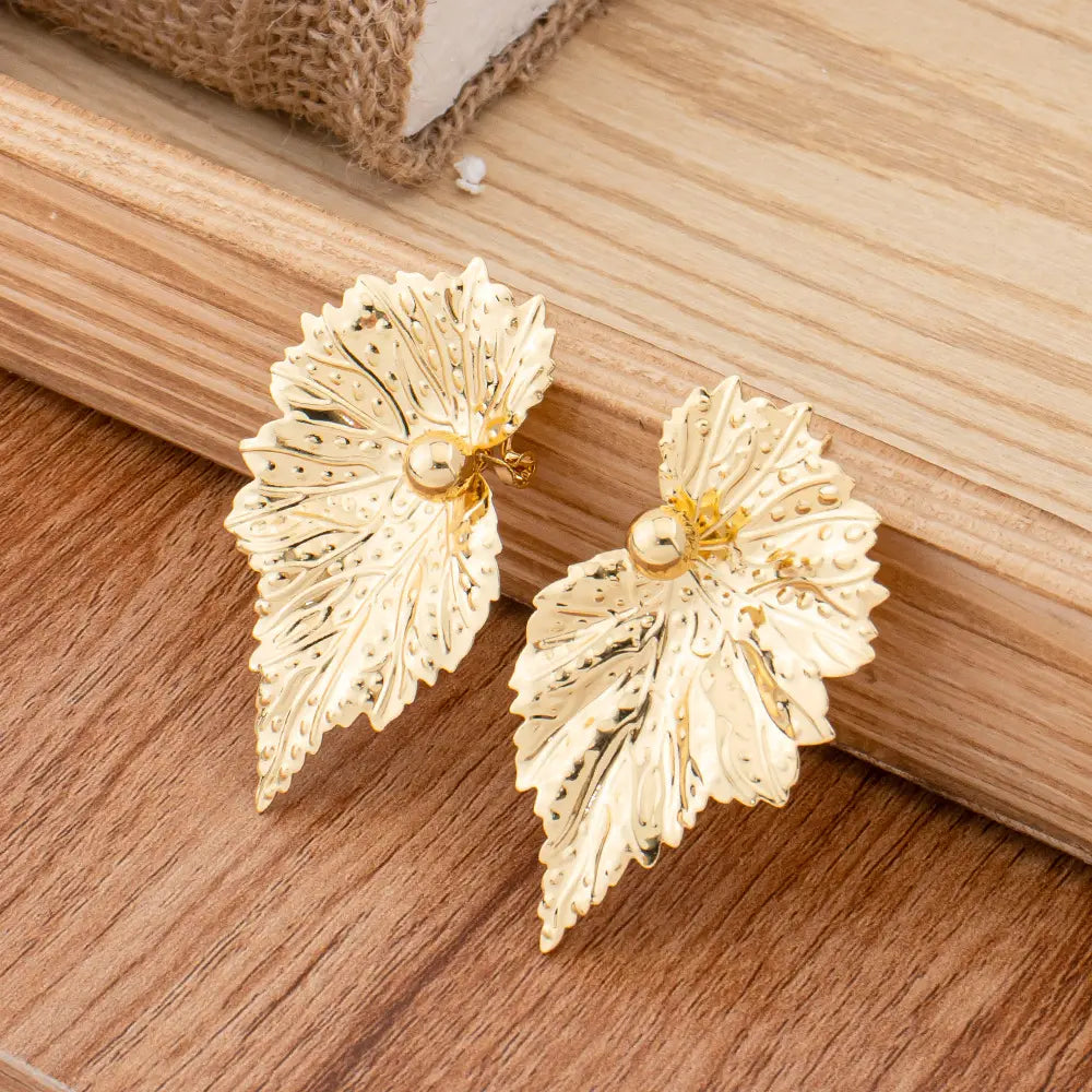Parure de bijoux en perles et feuilles d’or, comprenant des boucles d’oreilles à clous en forme de feuille d’or, avec des nervures complexes et une petite perle centrale.