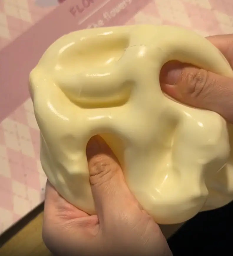 Un jouet à mâcher et à malaxer en forme de fromage jaune pâle, brillant, conçu pour soulager le stress, texture molle, avec une surface lisse légèrement irrégulière et de douces encoches, conçu pour apaiser le stress lié au jouet.