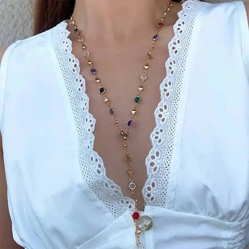 Eine zarte Halskette in Goldton, geschmückt mit farbenfrohen Edelsteinen in Rot, Grün, Blau und Lila, mit einem Kristallquasten-Statement-Design.