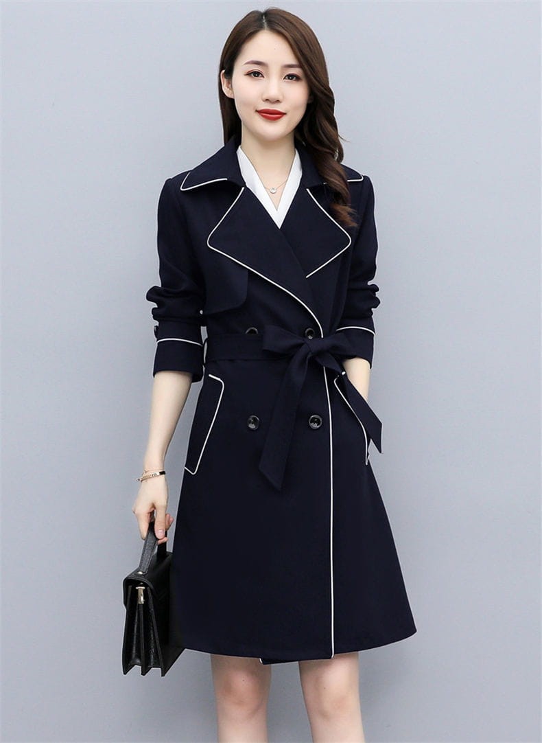Women double breasted trench coat in navy blue with white contrast stitching and a matching belt.