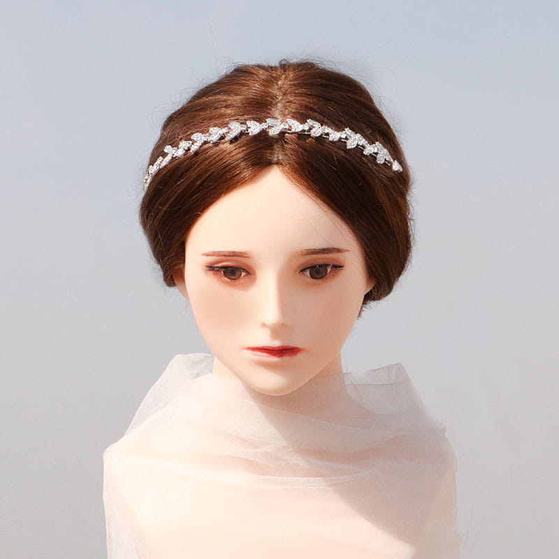 A delicate silver crystal leaf bridal headband adorned with sparkling rhinestones elegantly placed across a model’s brow as a wedding hair accessory.