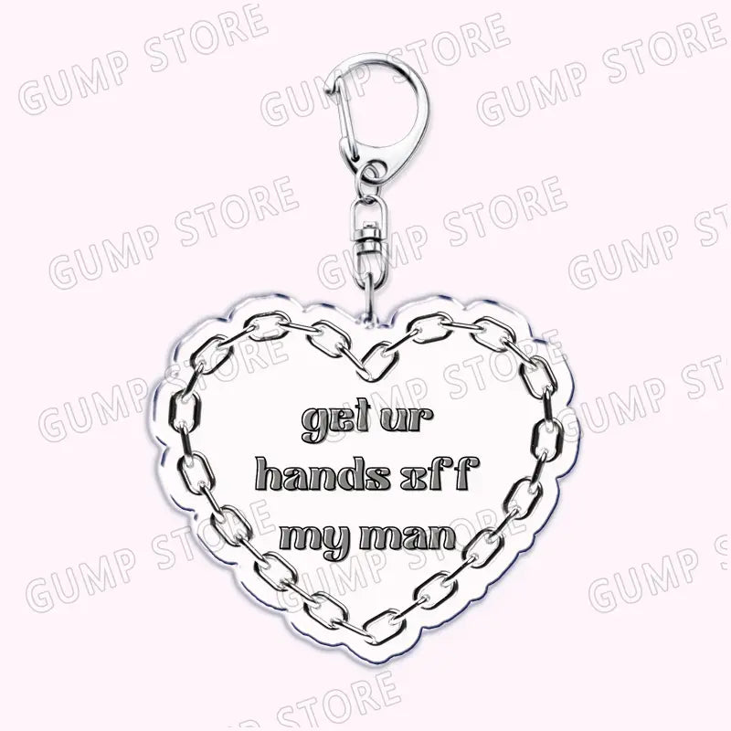 Silver heart-shaped acrylic Tate Mcrae keychain with a chain border and engraved phrase get ur hands off my man designed as a music fan gift.