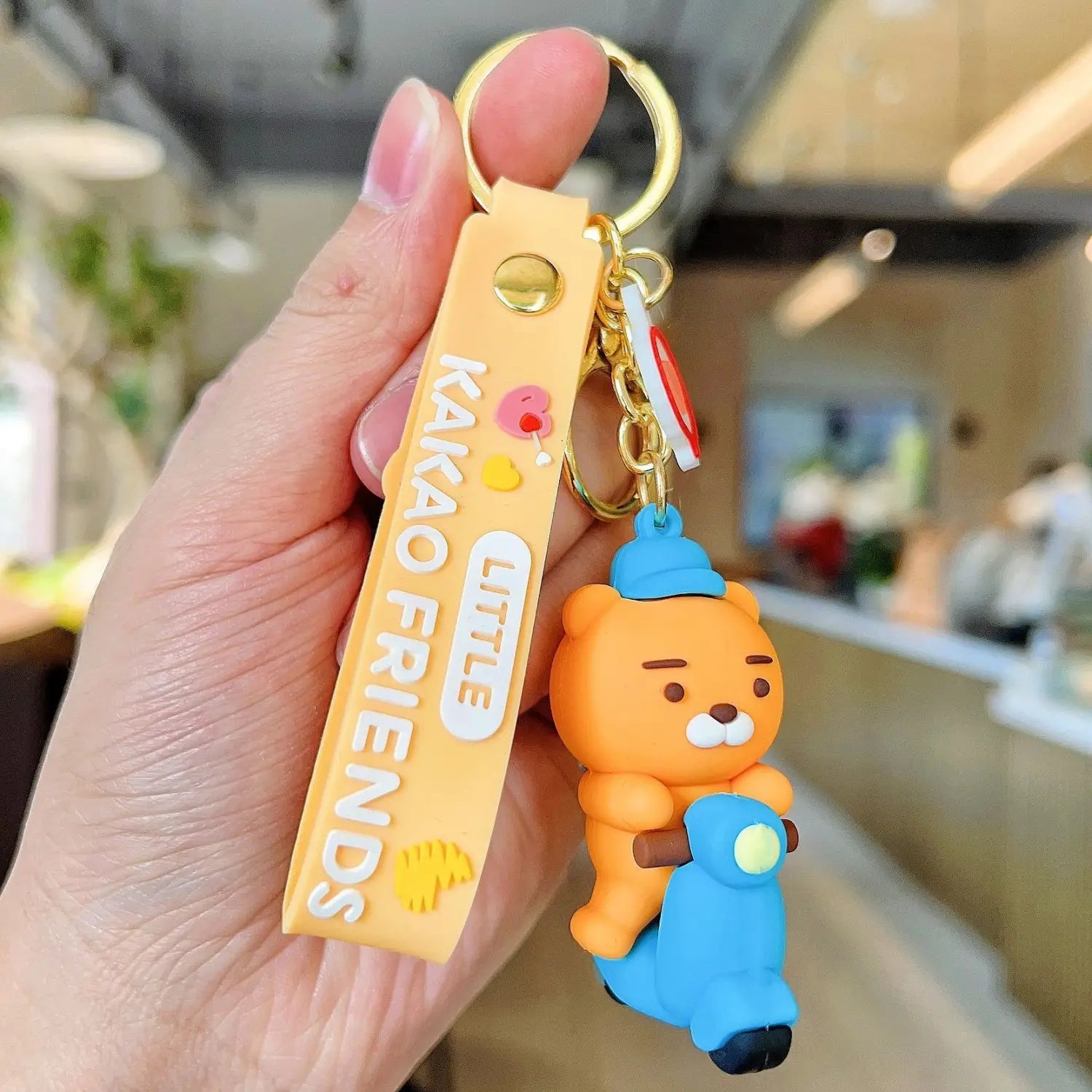 Orange silicone bear shaped Choonsik scooter keychain with blue scooter design and yellow strap reading little Kakao friends Korean viral gift.