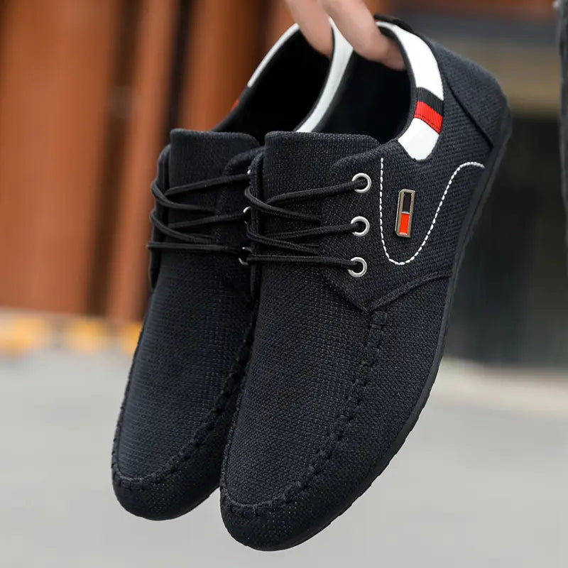 Men’s casual black canvas lace-up sneakers with white and red accents on the collar and a small rectangular logo patch designed for lightweight daily footwear.