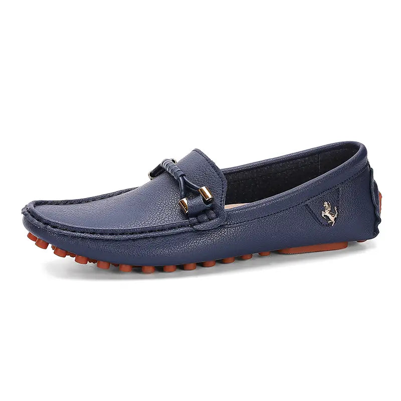 Les chaussures à enfiler habillées en cuir se portent sans effort avec des chaussures décontractées en cuir bleu marine, avec une surface texturée, une semelle en caoutchouc beige foncé et un emblème équestre ton or sur le côté.