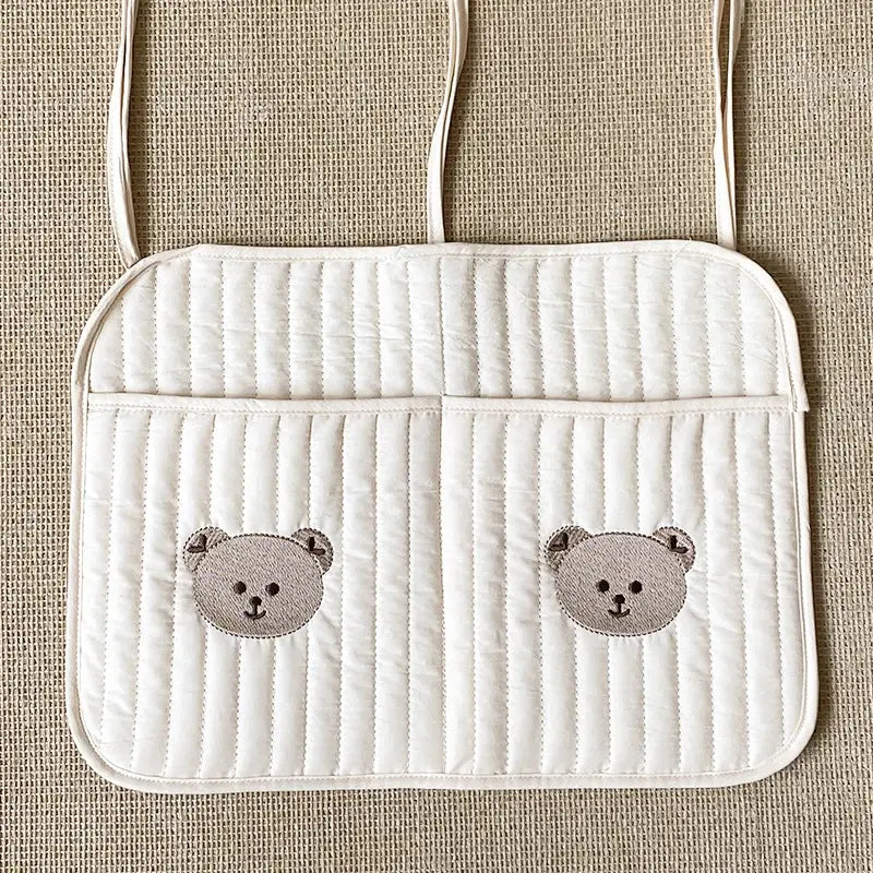 クマの刺繍が施されたキルティング製ベビーカー用オーガナイザー袋のための、布製の白いキルティングのカーシートオーガナイザーで、2つの刺繍入りグレーのクマの顔が付いています。