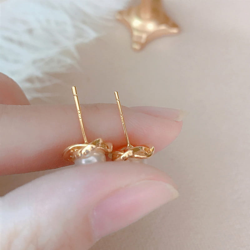 ゴールドトーンの中央パールアクセントを施した、繊細なフローラルデザインを特徴とする真珠のツイスト・ゴールドスタッドイヤリング。