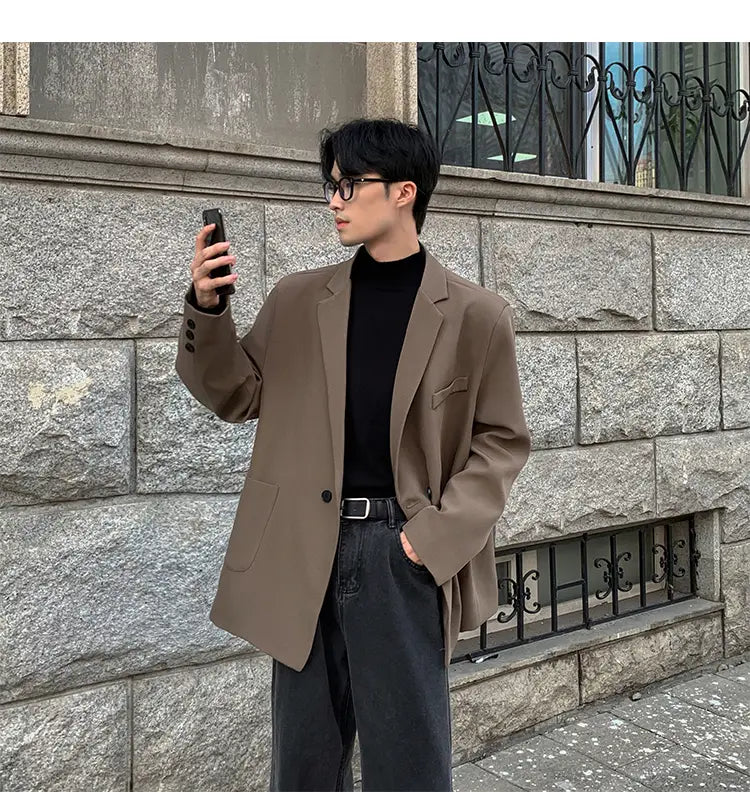 Una blazer de doble botonadura casual para hombre color canela, hecha de poliéster, con ajuste relajado, que presenta botones negros y bolsillos tipo cartera con solapa sutiles.