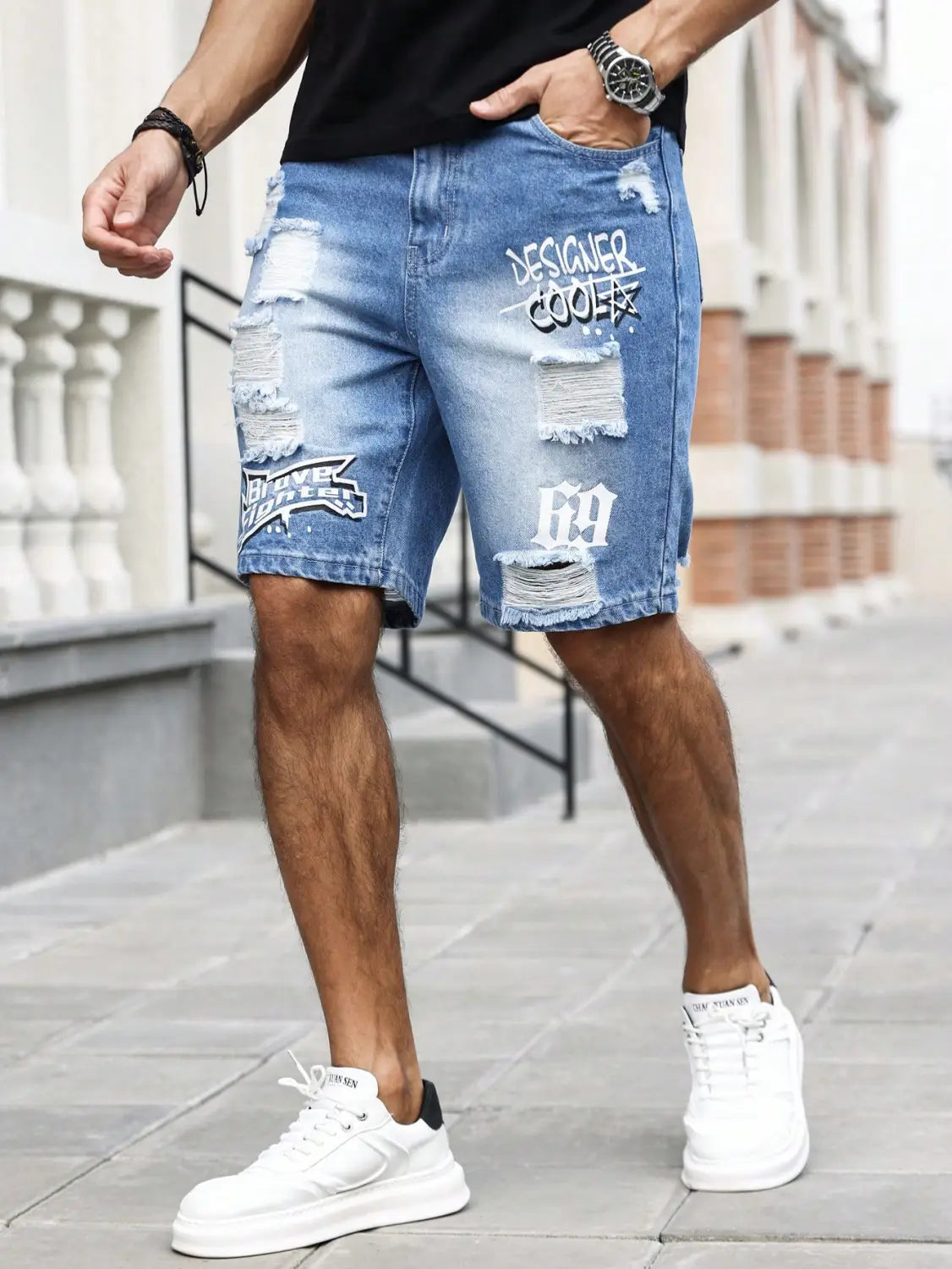 Shorts en jean bleu déchirés pour hommes, avec des genoux déchirés, des patchs de texte style graffiti blanc indiquant « designer cool » et « 69 », ainsi qu’un patch graphique noir et blanc sur la cuisse gauche, pour une tenue d’été.