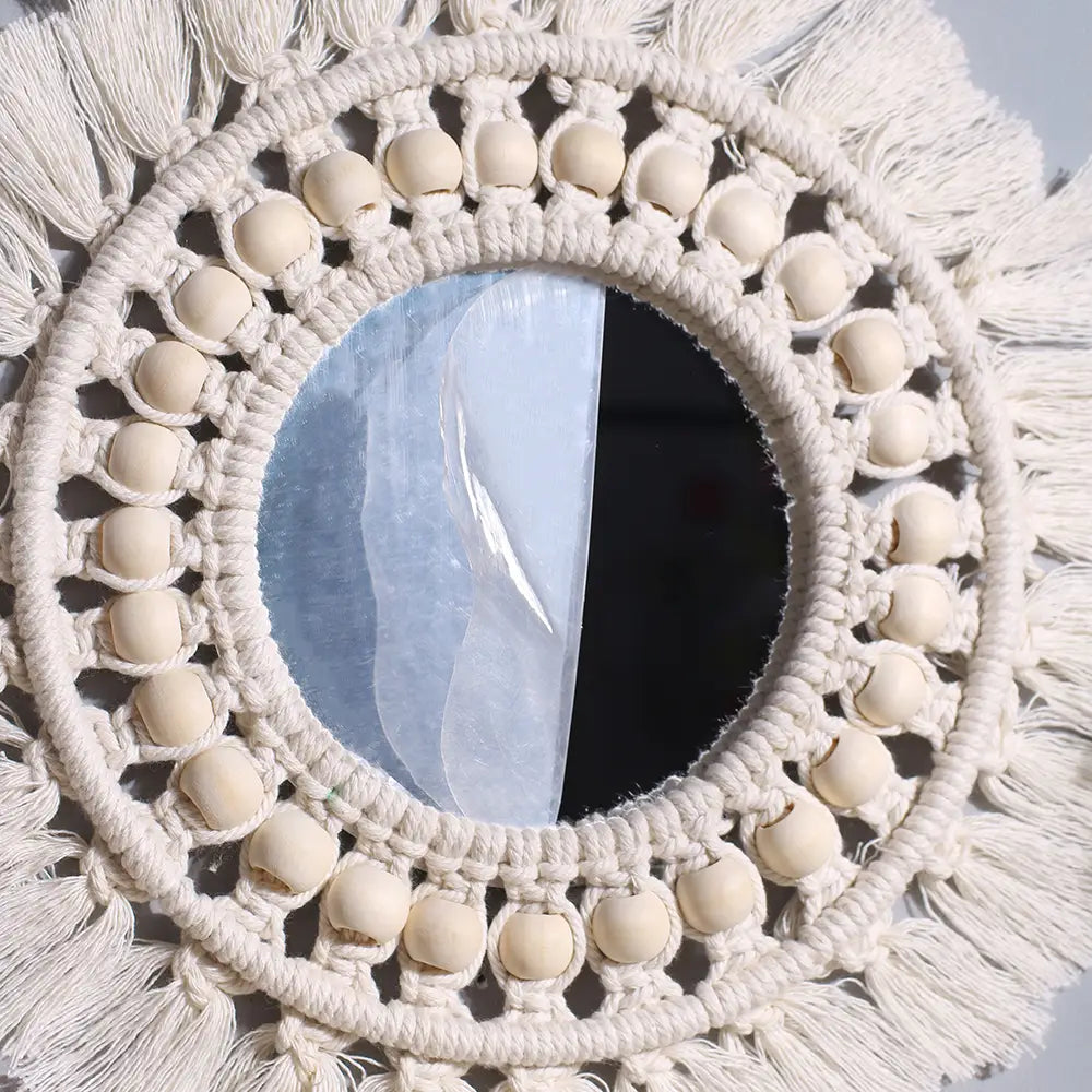 Cream-colored round macrame wall mirror with a decorative frame featuring wooden beads and tassels.