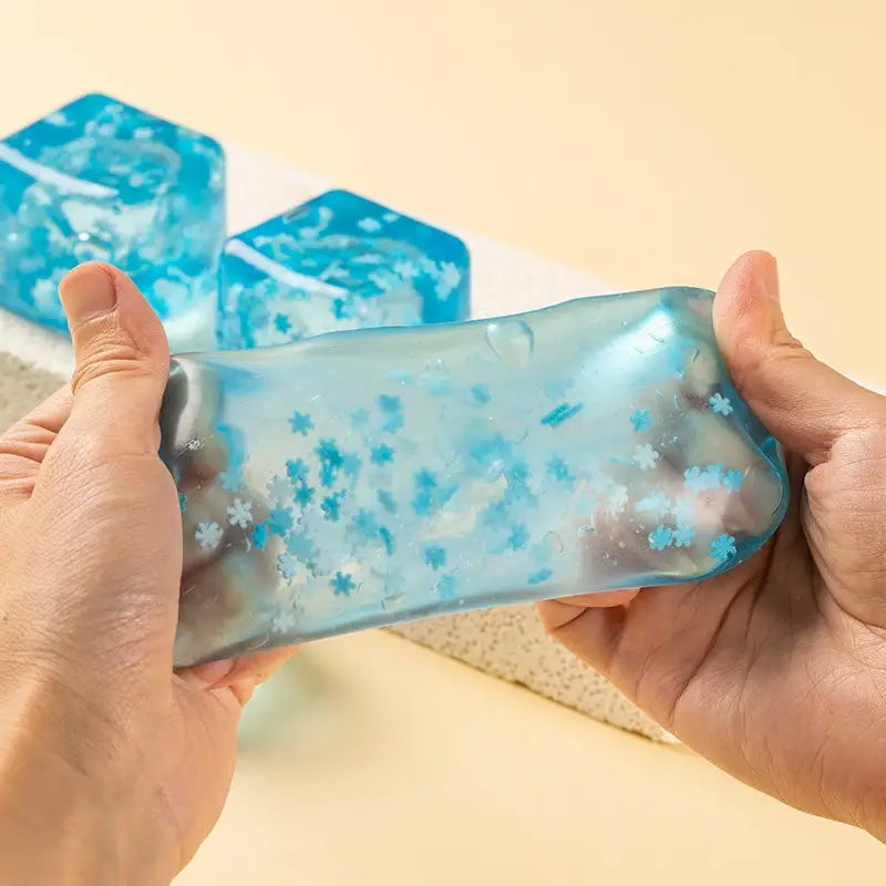 jouet de cube sphérique translucide bleu à faible rebond, visqueux et lent, avec des particules scintillantes en forme de flocons de neige intégrées, vu de face