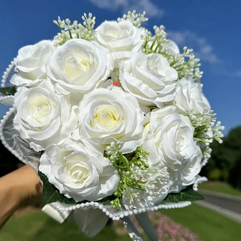 white silk rose wedding bouquet featuring delicate white artificial roses with subtle yellow centers, accented by greenery and a beaded lace and pearl ribbon wrap.