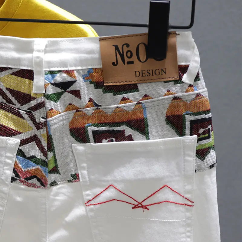 Men slim fit stretch embroidered white denim jeans featuring vibrant geometric pattern in earthy tones and red embroidery on front pocket.