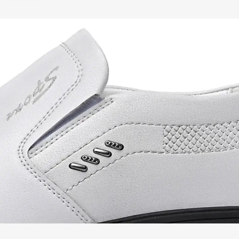 Zapato de conducción casual de cuero para hombre, tipo slip-on, en cuero blanco, con un diseño elegante que presenta costuras sutiles y acentos metálicos a lo largo del lateral.