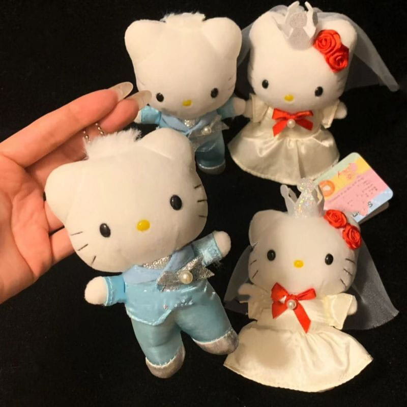 porte-clés en peluche couple de mariage Hello Kitty, représentant des figurines en peluche blanches habillées d’un costume bleu clair avec des accents argentés, et d’une robe de satin blanche ornée de roses rouges et d’un voile.
